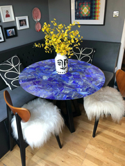 Stunning round blue lapis-inspired table with a glossy mosaic design, featuring vibrant yellow floral decor in a unique vase.