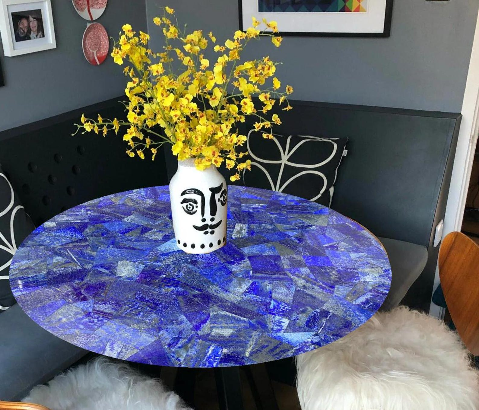 Stunning round blue lapis-inspired table with a glossy mosaic design, featuring vibrant yellow floral decor in a unique vase.