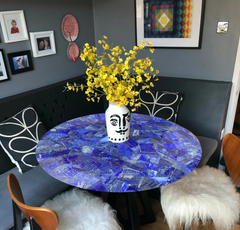 Stunning round blue lapis-inspired table with a glossy mosaic design, featuring vibrant yellow floral decor in a unique vase.